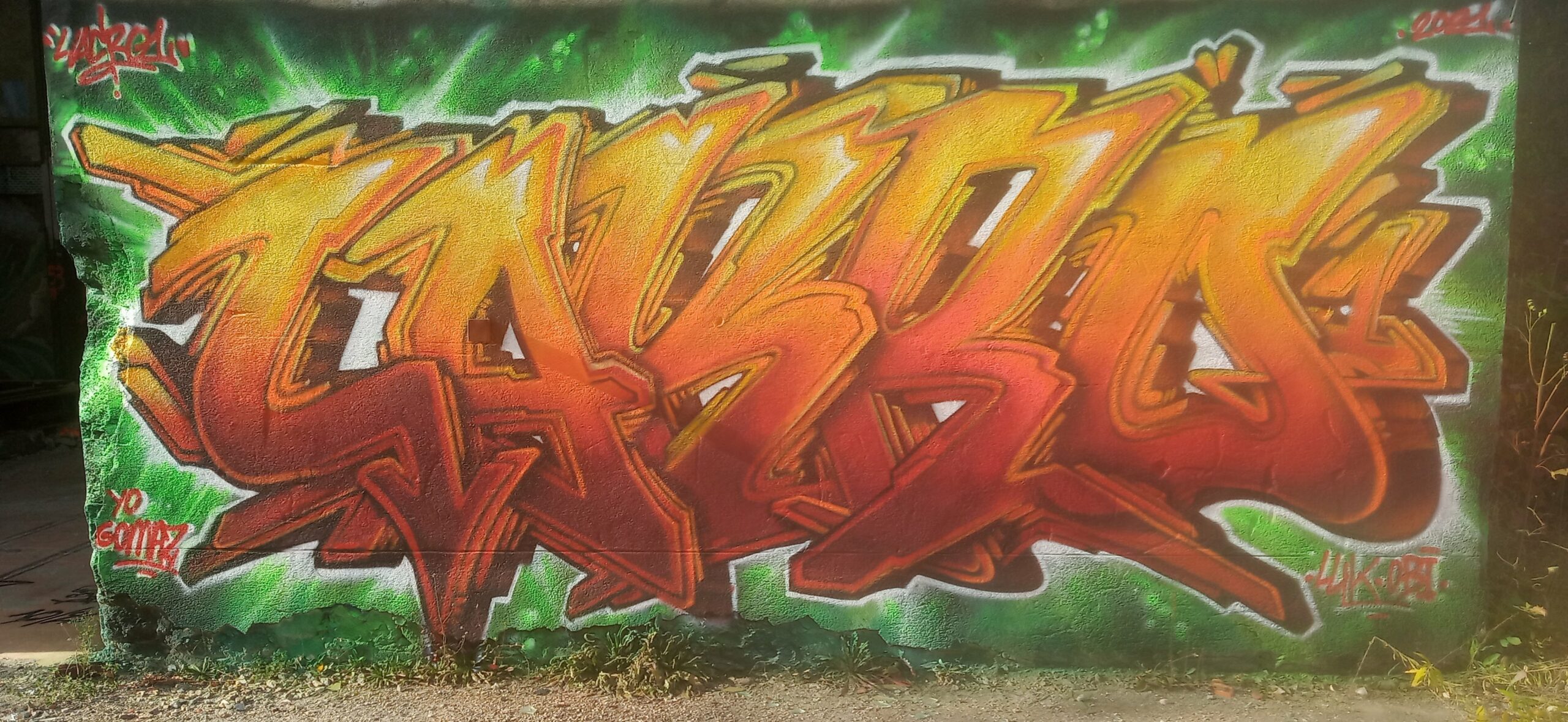 Lettrage GRAFFITI 2d “LAKRO 1" sur le terrain d'Unieux dégradé flamme sur fond vert et noir